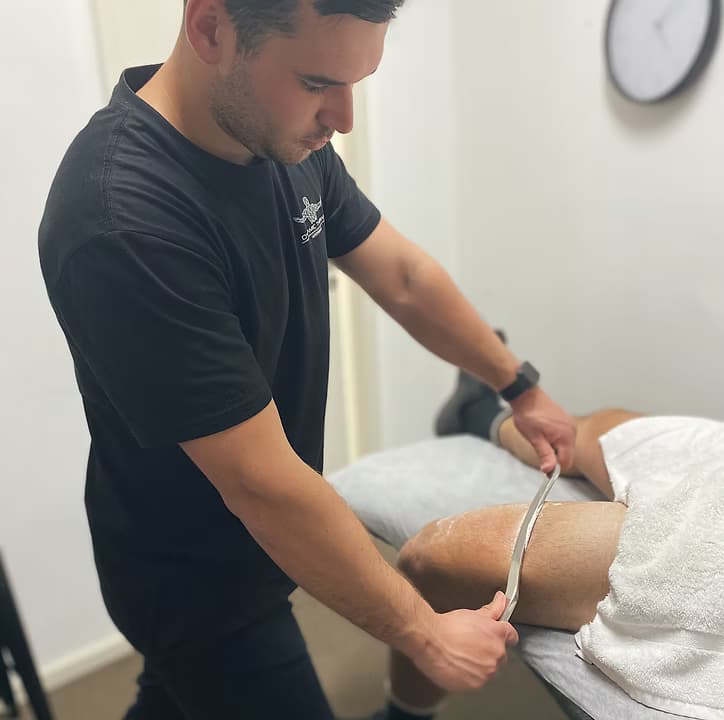 Myotherapist in a Dynamic Therapy shirt assessing a client's back before treatment